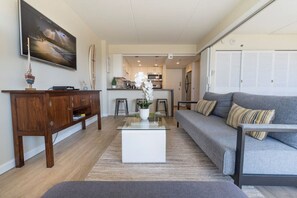 Un salon moderne avec un canapé gris, un buffet en bois et une table basse agrémentée d’un vase de fleurs.