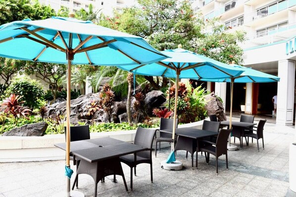 Outdoor seating with umbrellas, a landscaped garden, and a building in the background.