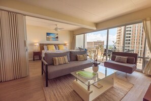 Habitación de hotel moderna con una cama grande, un sofá, una mesa de centro de vidrio y vistas a la ciudad a través de amplias ventanas.