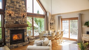 Un salón espacioso con chimenea de piedra, ventanas amplias y comedor con vistas al exterior.