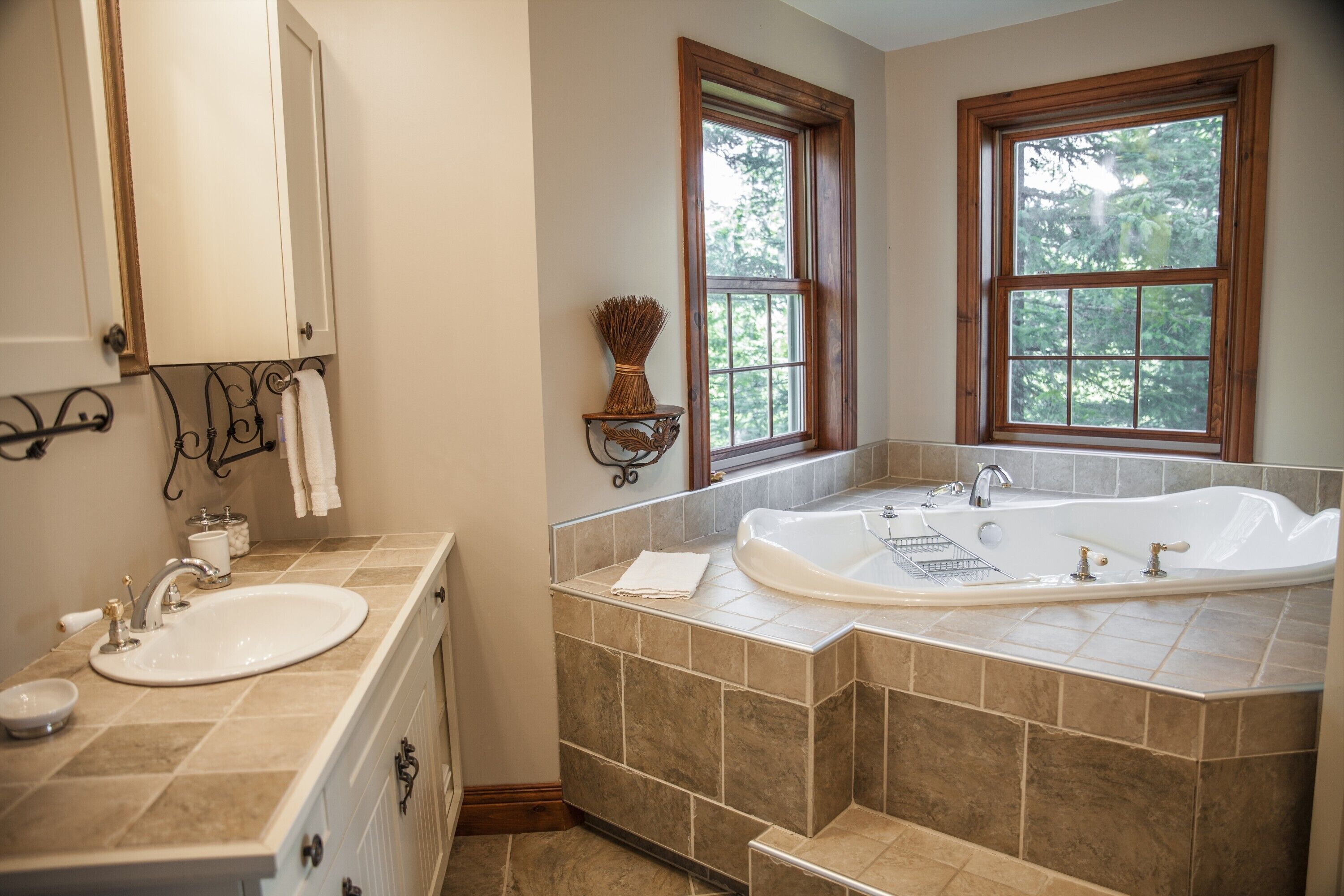 A bathroom with a large bathtub, a sink, and a mirror. There are two windows providing natural light.