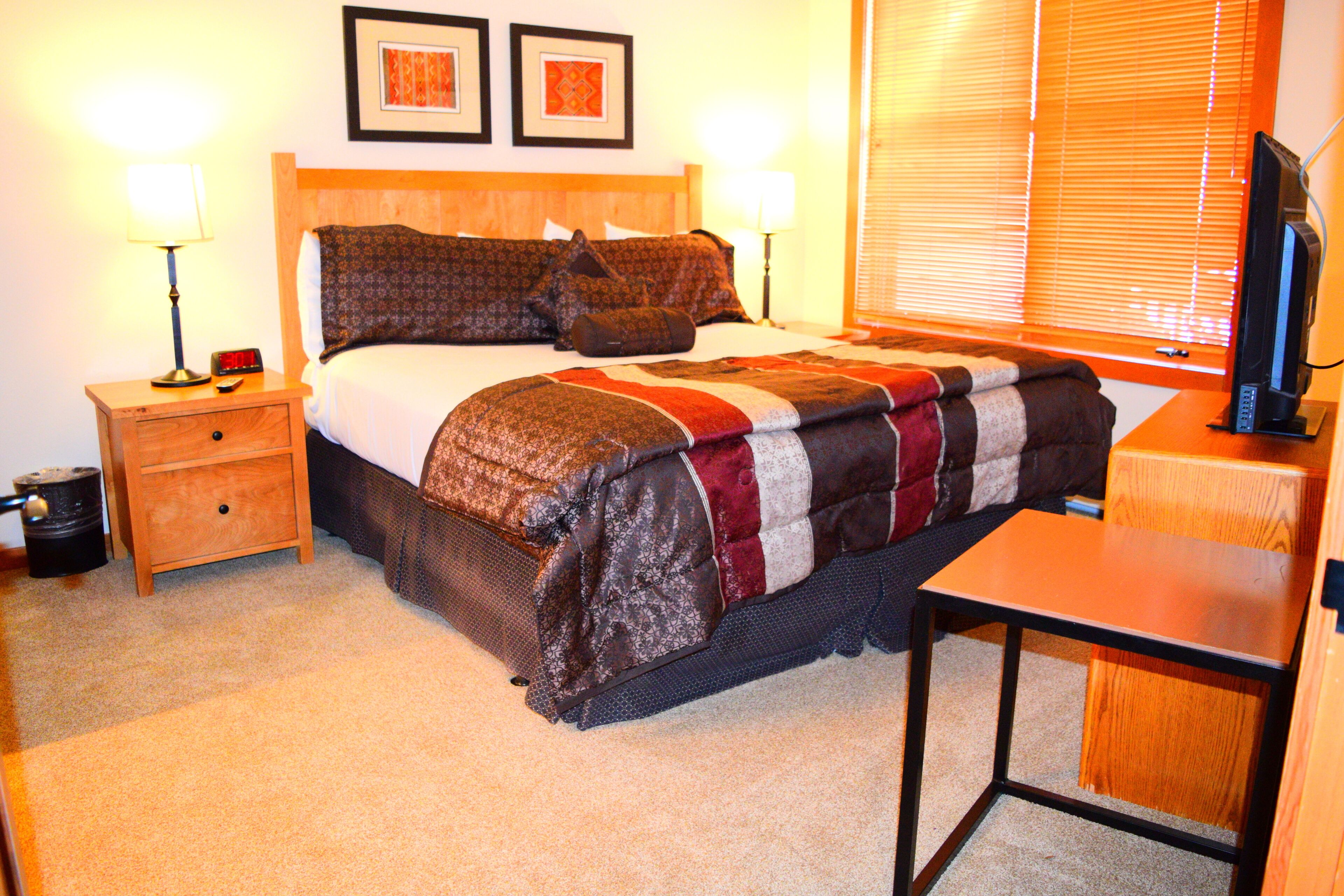 A hotel room with a bed, bedside tables, a desk, a television, and two framed pictures on the wall.