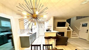 A modern kitchen with a central island, a dining area with a wooden table, and a staircase leading to an upper level.