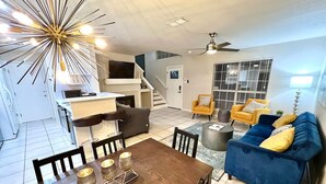 A modern living room with a dining area, a blue sofa, and a staircase leading to an upper level.