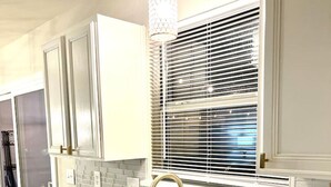A modern kitchen with white cabinetry, a double sink, and a window with blinds.
