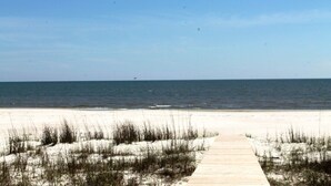 A wooden boardwalk leading to a sandy beach with sparse vegetation.