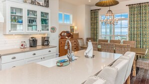A spacious kitchen with a central island, white cabinetry, and a dining area with wicker furniture.