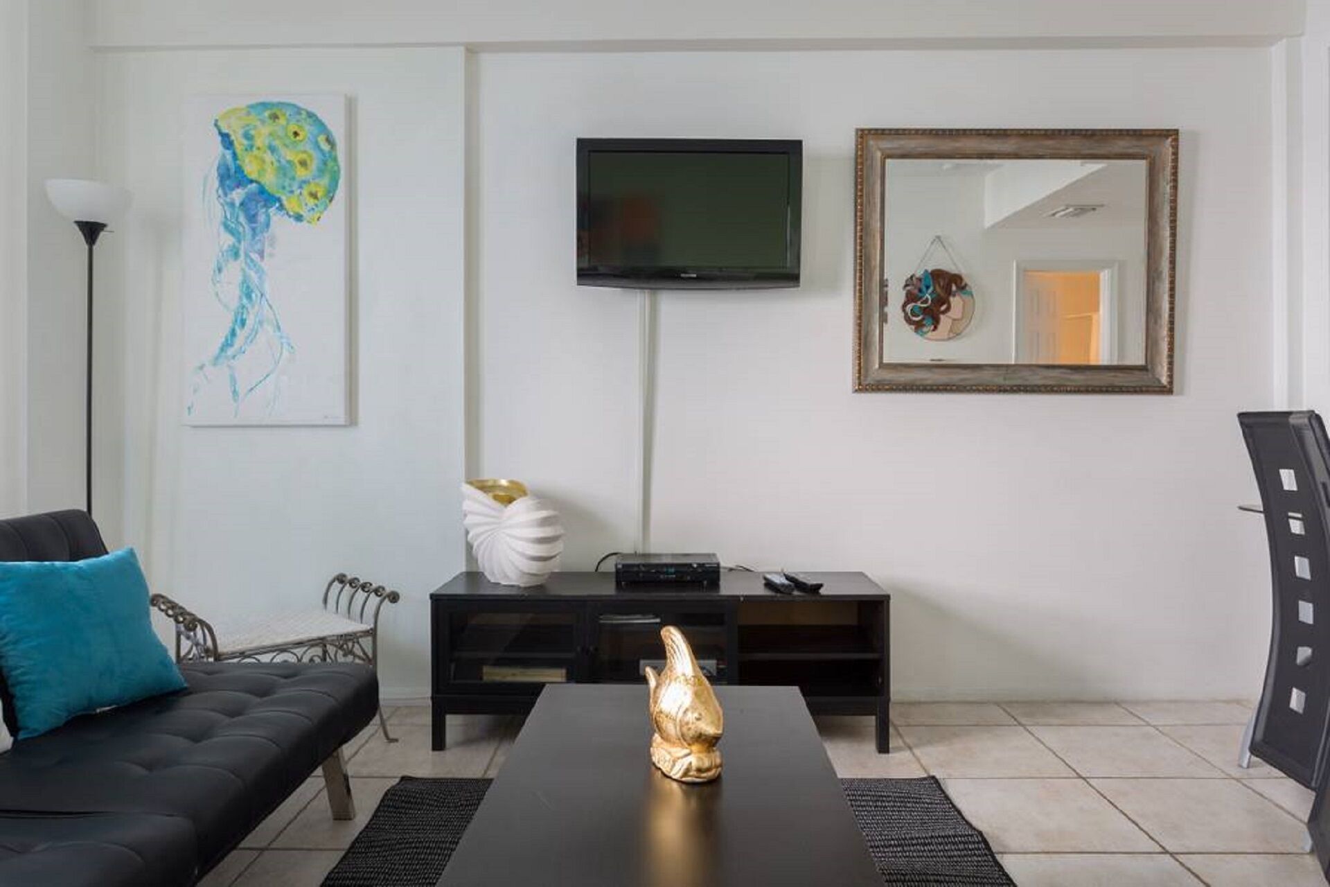 A modern living room with a black sofa, a coffee table, a flat-screen TV, a decorative mirror, and a wall art piece.