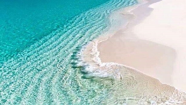 Una platja amb aigua turquesa cristal·lina i sorra blanca.