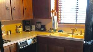 A kitchen with wooden cabinets, a dishwasher, a coffee maker, and a window with blinds. - Fully Furnished Two Bedroom Farm House, "The Little House" Has Everything ! (Delight)