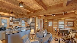 A spacious log cabin interior with a central island kitchen, a cozy seating area with a sofa and chairs, and a dining table. - Cozy Log Cabin, Mountain views, HOT TUB, & Fire Pit- accepting renters! (Zionville)