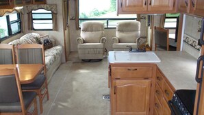 A compact RV interior with a kitchenette, dining area, and seating space.