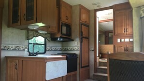A compact RV kitchen with wooden cabinets, a microwave, and a stove.