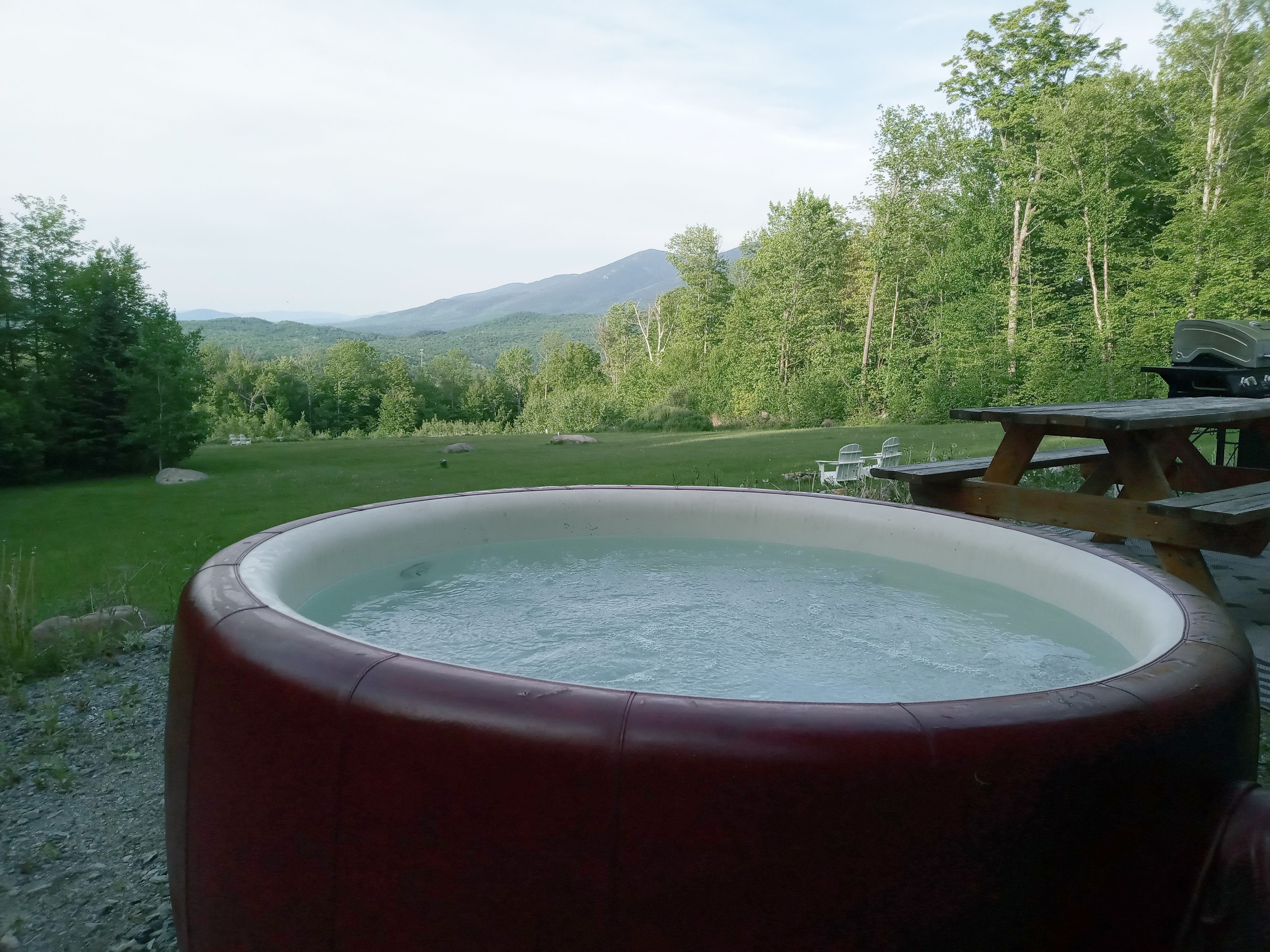 Una vasca idromassaggio in un ambiente naturale, con un tavolo da picnic e sedie nelle vicinanze.
