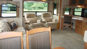 A compact RV interior with two reclining chairs, a small desk, and a couch.