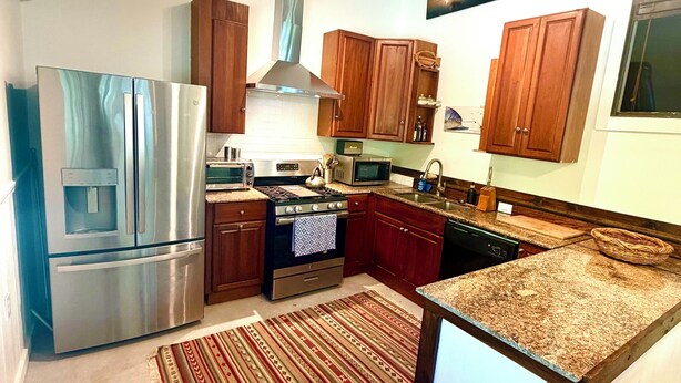 A modern kitchen with stainless steel appliances, wooden cabinets, and a granite countertop.