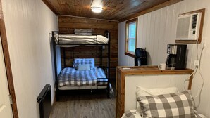 A compact room with bunk beds, a wooden ceiling, a window, a coffee maker, and a wall-mounted air conditioner.