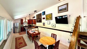A modern kitchen with stainless steel appliances, a dining area with a wooden table and chairs, and a hallway with artwork on the walls.