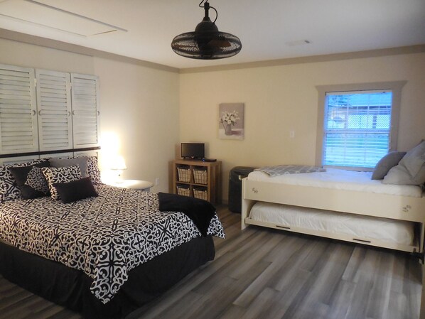 A bedroom with a bed, bedside table, lamp, TV, and a window with blinds.