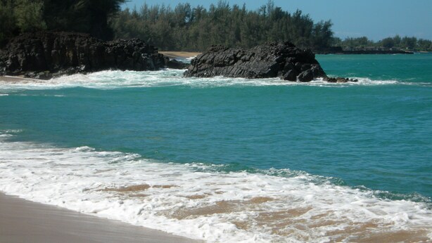 Une plage bordée d’une eau turquoise et limpide et parsemée de rochers.