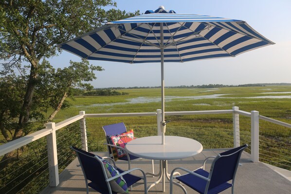 A patio with a table and chairs, an umbrella, and a view of a green landscape. - Marsh--Mellow in Wild Dunes Resort, 20 mins from historic Charleston! (Isle of Palms)