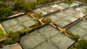 Ovenfra taget billede af et tenniskompleks med flere baner, omgivet af træer og grøn bevoksning.