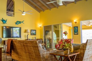 A bright yellow room with wicker furniture, a flat-screen TV, and decorative fish wall art. - Villa Tryst, Waterfront Hull Bay Beach (Northside)