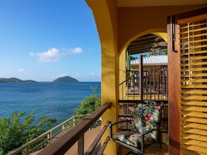 A balcony with a view of the sea and distant islands, wooden railings, and a chair with a floral pattern. - Villa Tryst, Waterfront Hull Bay Beach (Northside)