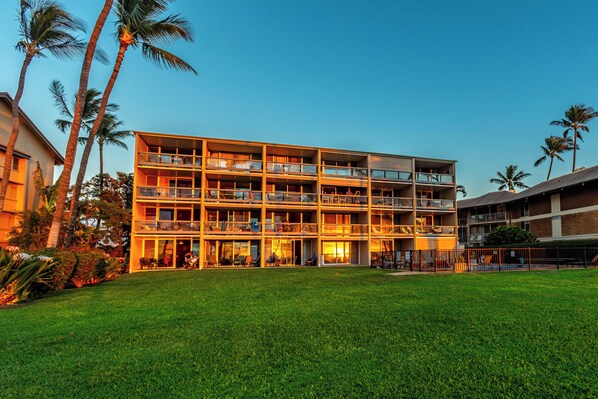 A multi-story hotel with balconies, a grassy lawn, and palm trees.
