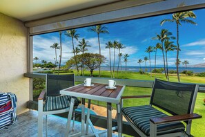 A balcony with a table and chairs, overlooking a tropical landscape with palm trees and a view of the ocean.