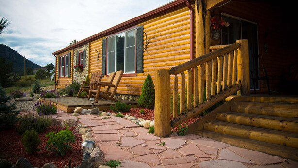 Une cabane en rondins dotée d’une terrasse en bois, d’un espace salon extérieur et d’un chemin en pierre menant à l’entrée.