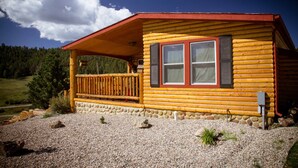 Une cabane en rondins dotée d’une terrasse en bois, d’un porche et de fondations en pierre.