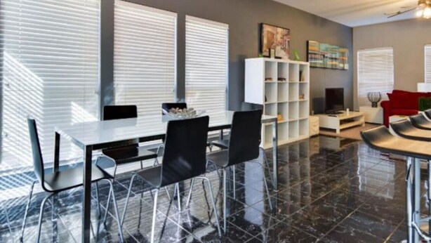 A modern living room with a dining area, large windows, and a white bookshelf. - City View! Walk 2 AlamoDome/RiverWalk. Spurs game! (San Antonio)