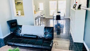 A modern living room with a black leather sofa, a coffee table, and a dining area with bar stools. - City View! Walk 2 AlamoDome/RiverWalk. Spurs game! (San Antonio)