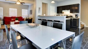 A modern kitchen with dark cabinets and a white countertop, a dining area with a white table and chairs, and a red sofa in the living area. - City View! Walk 2 AlamoDome/RiverWalk. Spurs game! (San Antonio)