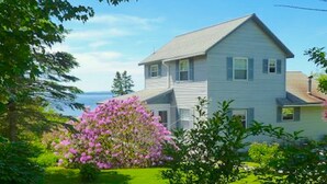 A two-story house with a sloped roof, surrounded by lush greenery and flowering bushes.