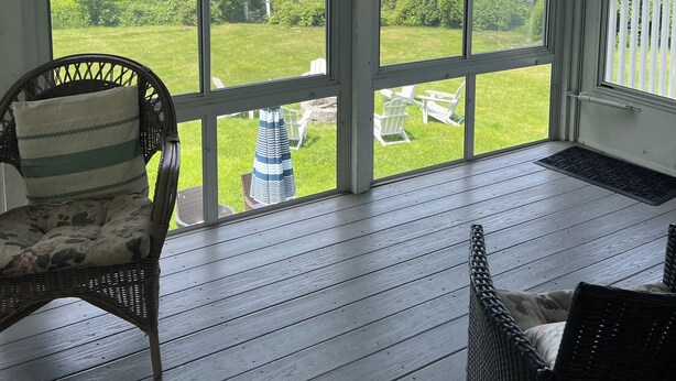 A covered porch with wicker chairs, a view of a lake, and a hanging lantern.