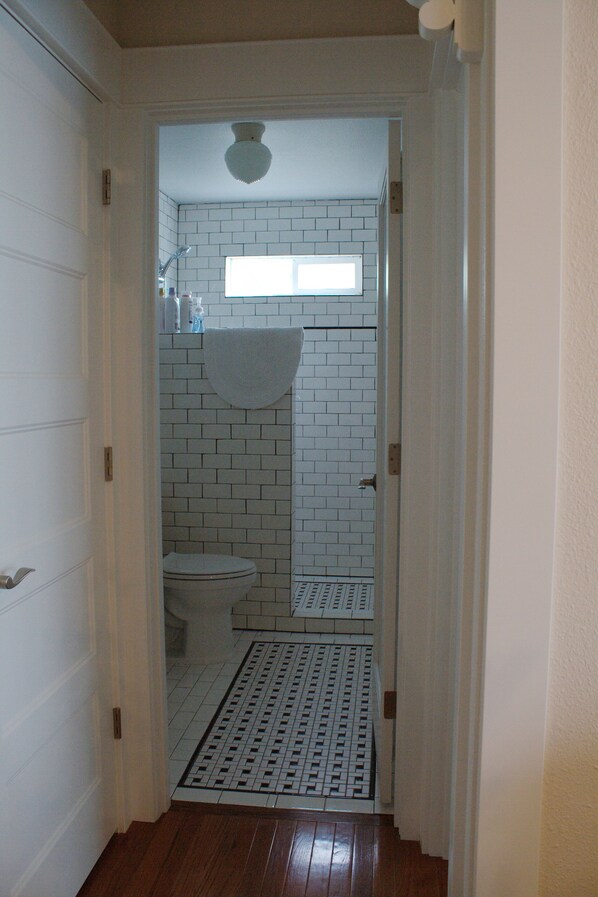 A narrow hallway leading to a bathroom with white tiled walls, a white toilet, and a shower area. - New High End Guesthouse in Warm Beach, Stanwood, WA. (Stanwood)