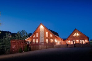 A two-story log cabin with a prominent central chimney, a covered porch, and a well-lit facade.