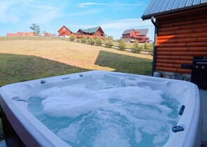 A hot tub with a view of a wooden cabin and red buildings in the background.