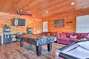 A wooden interior with a pool table, a sofa, and a television.