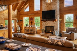 A cozy cabin interior with a stone fireplace, wooden beams, and large windows. - Spacious 5BR Mountain Escape Mt. Airy | With Views (Dobson)