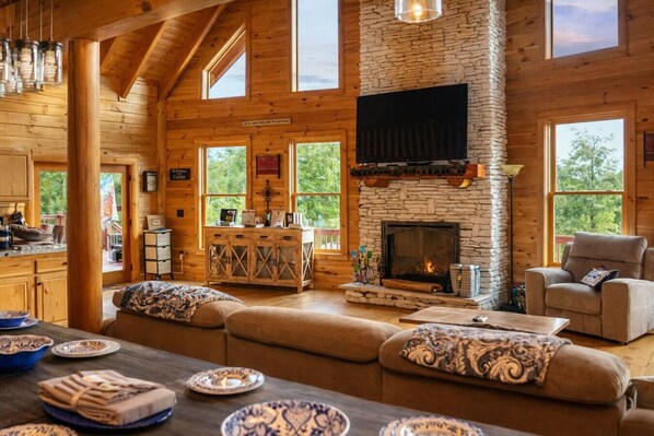A cozy cabin interior with a stone fireplace, wooden beams, and large windows.
