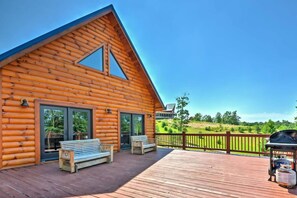 A log cabin with a deck, two benches, and a grill.