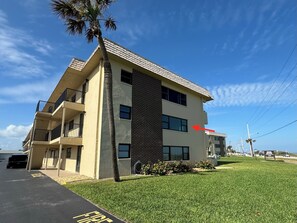 Un edificio de varios pisos con techo plano, una palmera y un estacionamiento.