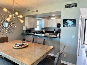 Una cocina moderna con armarios blancos, una zona de comedor con mesa de madera y un letrero que indica 'Surfer Lounge'.