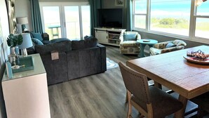 Una sala de estar con sofá, televisor, mesa de comedor y vista al exterior.