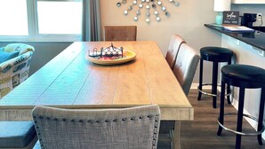 Un comedor con mesa de madera, sillas tapizadas, un adorno en la pared y una lámpara colgante.