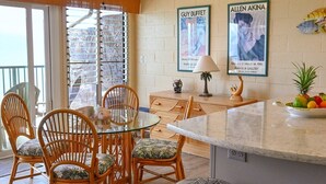 A dining area with wicker chairs and a glass table, a ceiling fan, and a wall with two framed pictures.