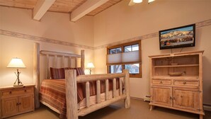 A bedroom with a wooden bed, two bedside tables, a wooden cabinet, and a television on the wall.